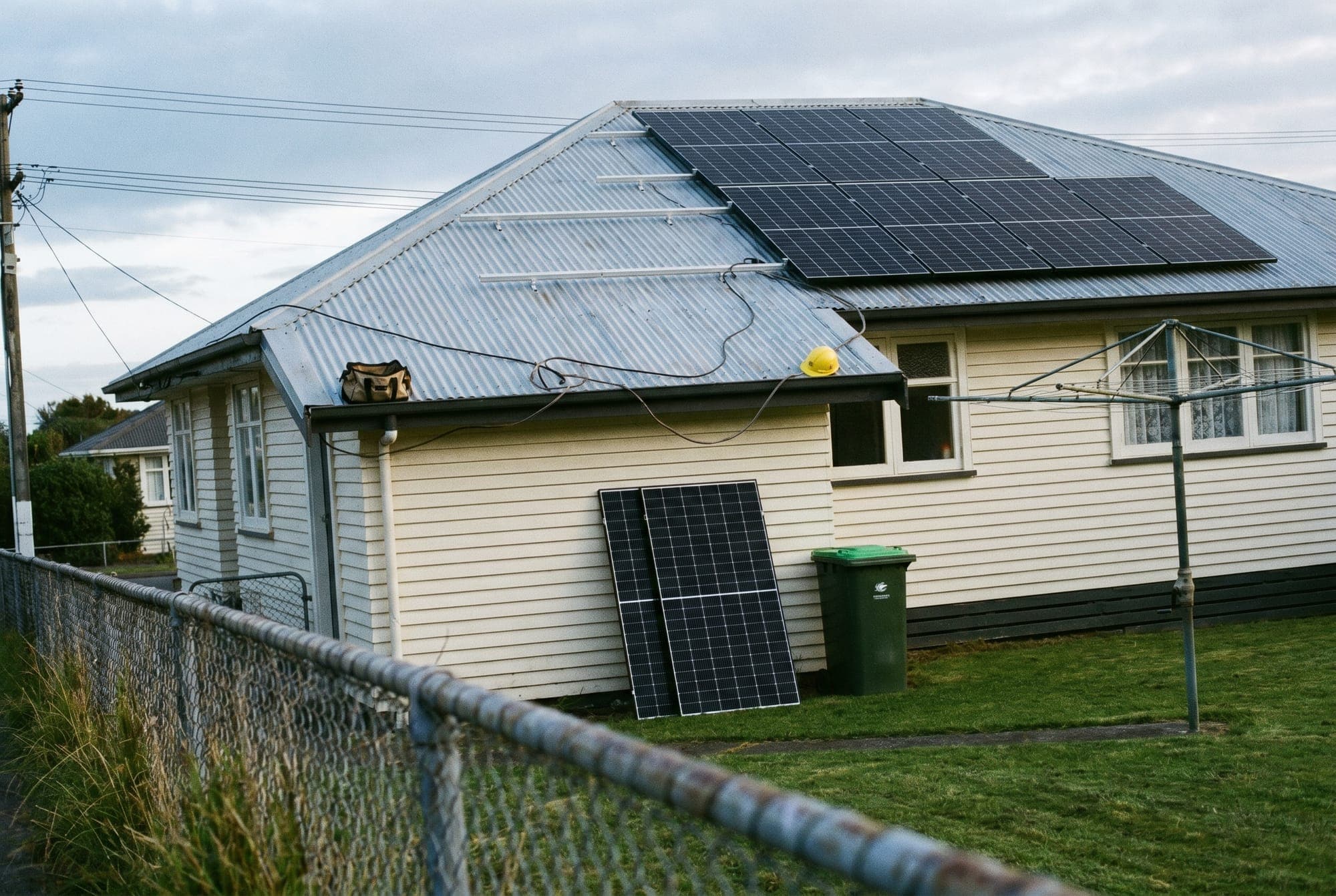 A New Zealand homeowner sitting on their front porch reading a solar contract document, a half-installed solar array visible on the roof