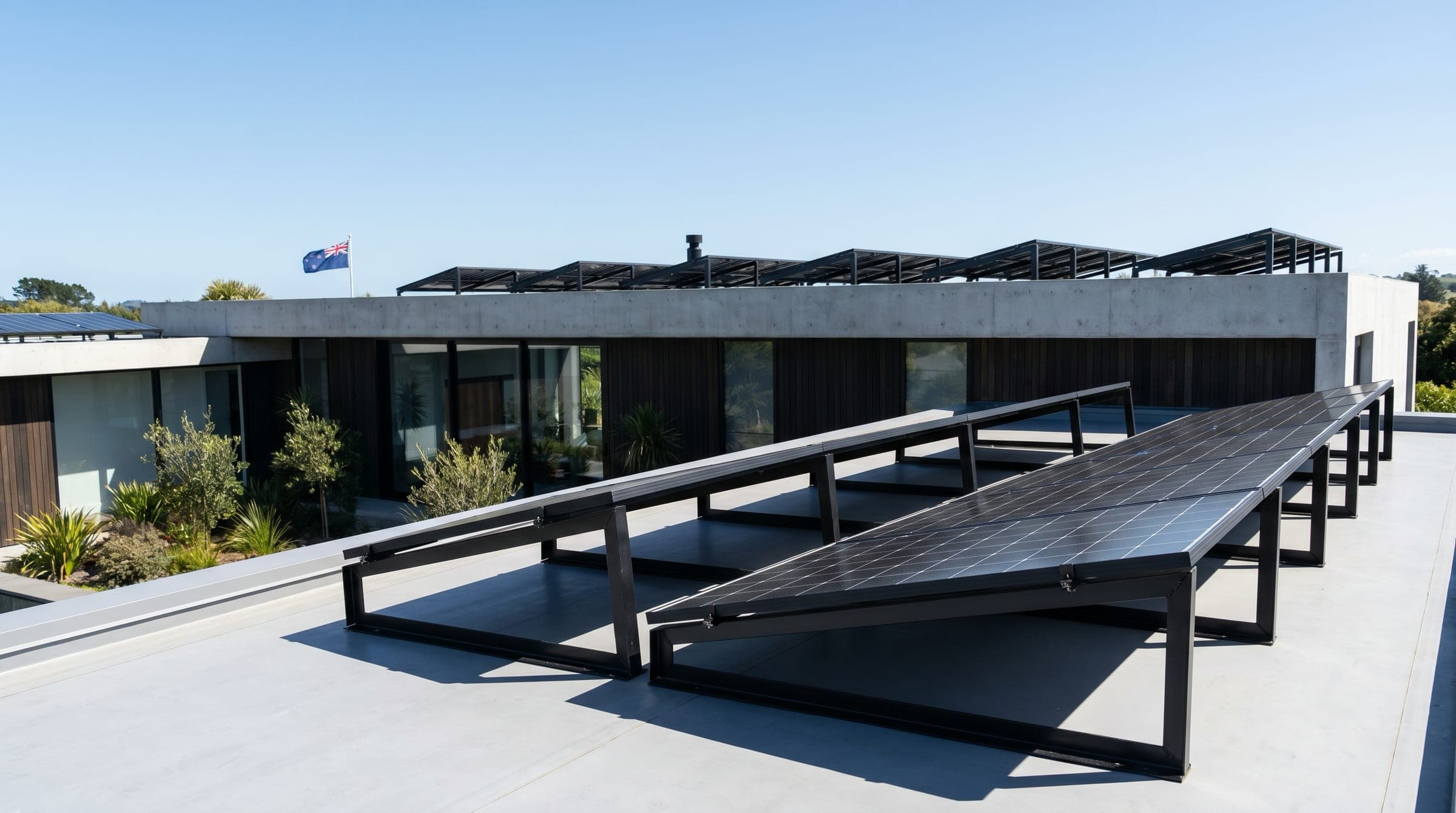 A New Zealand flat-roof building with an array of all-black solar panels mounted on visible tilt frames angled toward the north sun.